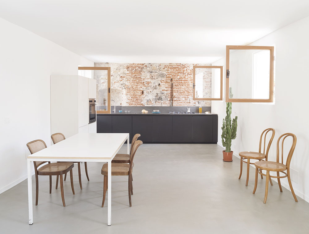 En la cocina, con el fondo de ladrillo visto, mesa de comedor con sillas Thonet